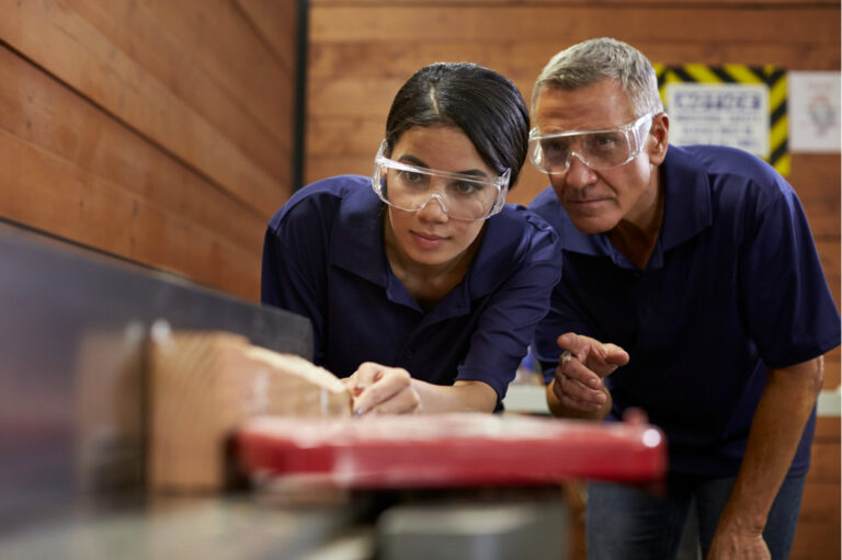 Image montrant un homme apprenant à une apprentie le fonctionnement d'une machine à découper du bois. Image d'accueil du site internet d'Avenir Pro